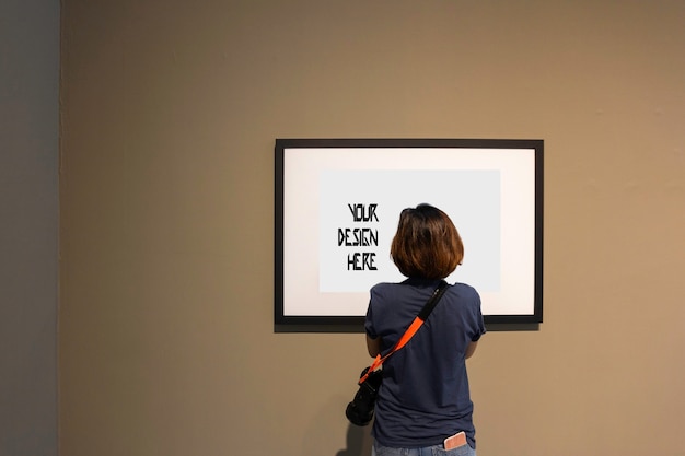 Mulher está olhando para moldura em branco na parede na Galeria de arte