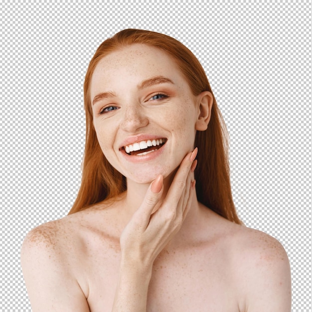 Nahaufnahme einer jungen schönen rothaarigen Frau, die vorne lächelt, perfekte saubere Haut auf dem Gesicht berührt und glücklich aussieht, nackt über einer weißen Wand stehend