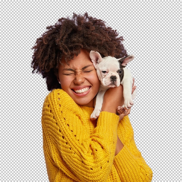 O dono do cão e seu animal de estimação Uma menina etnica feliz e encaracolada segura um cachorrinho bonito perto do rosto Exprime amor e cuidado para o animal doméstico Compra cão da raça favorita Ri-se tem os olhos fechados de prazer
