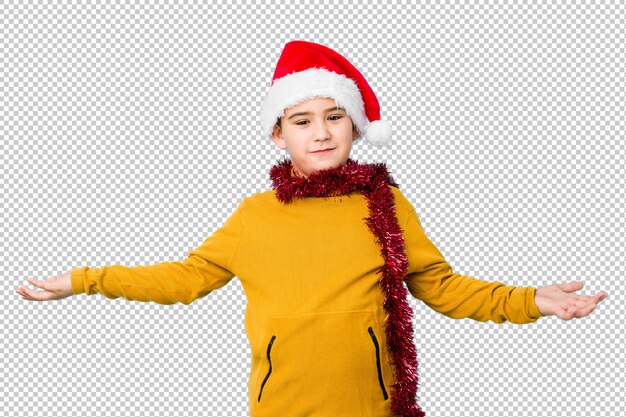 O rapaz pequeno que comemora o dia de natal que desgasta um chapéu de santa isolou mostrar uma expressão bem-vinda.