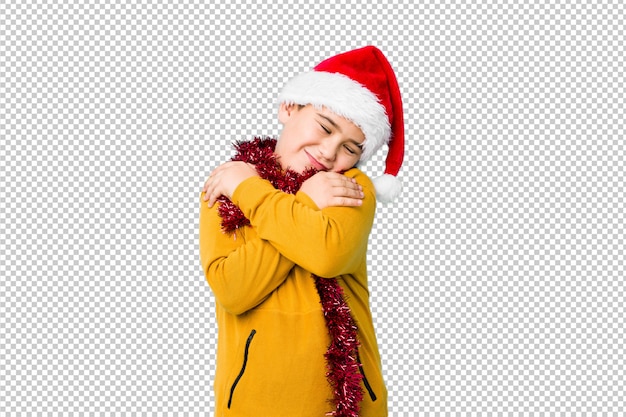 PSD o rapaz pequeno que comemora o dia de natal que veste um chapéu de santa isolou abraços, sorrindo despreocupado e feliz.