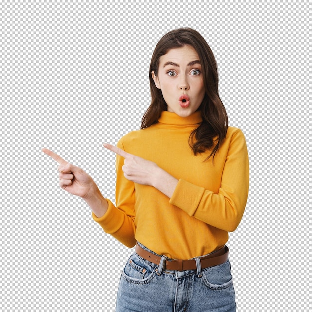 On dirait cool intrigué et excité jeune femme pointant des doigts à gauche dire wow et regardant fixement la caméra impressionné debout dans un pull jaune sur un fond blanc