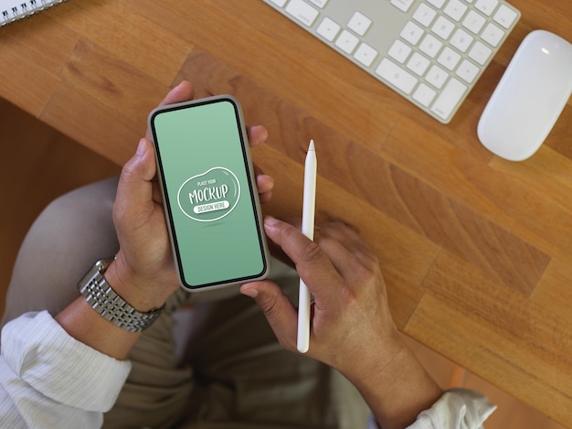 Overhead-Schuss von männlichen Arbeiterhänden, die Schein-Smartphone halten, während sie am Schreibtisch arbeiten