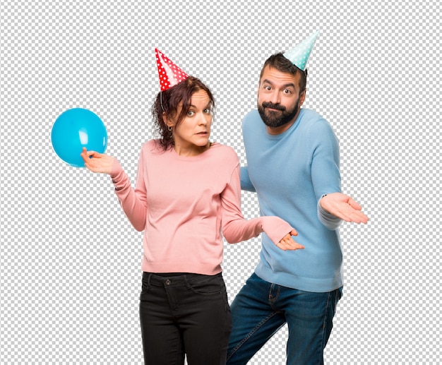 Paare mit den ballonen und geburtstagshüten, die zweifel machen, während sie schultern anhebt