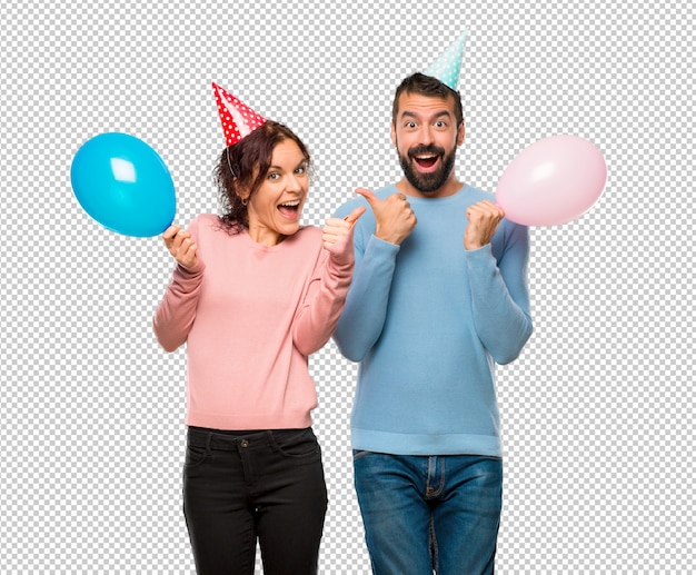 Pareja con globos y sombreros de cumpleaños dando un pulgar arriba gesto