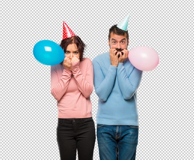 Pareja con globos y sombreros de cumpleaños es un poco nervioso y asustado poniendo las manos en la boca