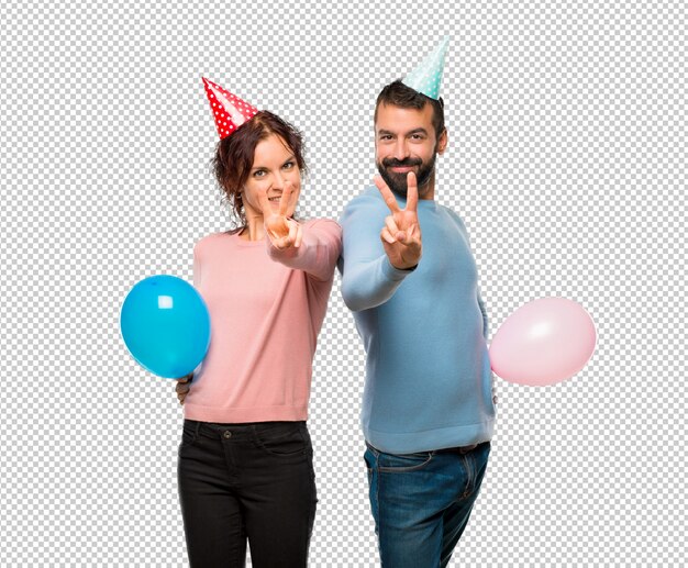 PSD pareja con globos y sombreros de cumpleaños sonriendo y mostrando el signo de la victoria