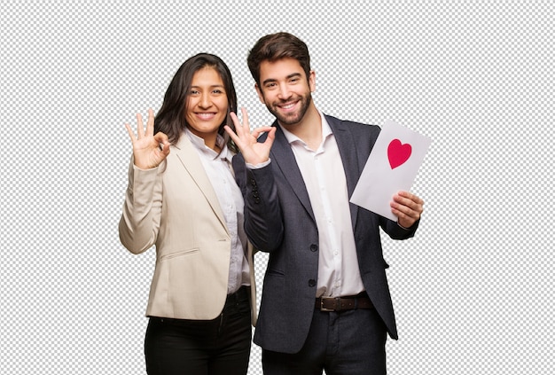 Pareja joven en el día de san valentín alegre y confiada haciendo gesto aceptable