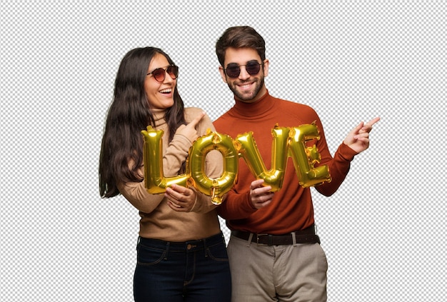 Pareja joven en el día de san valentín sonriendo y apuntando hacia el lado