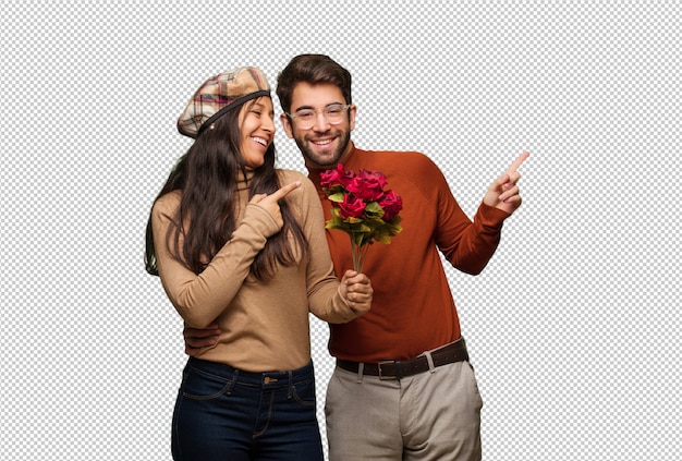 Pareja joven en el día de San Valentín sonriendo y apuntando hacia el lado