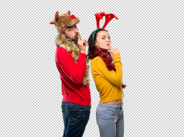 Pareja vestida para las fiestas navideñas mostrando un signo de boca cerrada y gesto de silencio