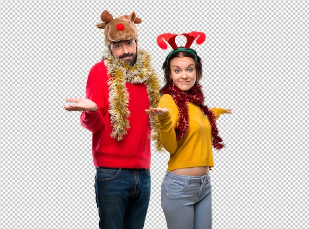 Pareja vestida para las vacaciones de navidad haciendo gestos de dudas mientras levanta los hombros