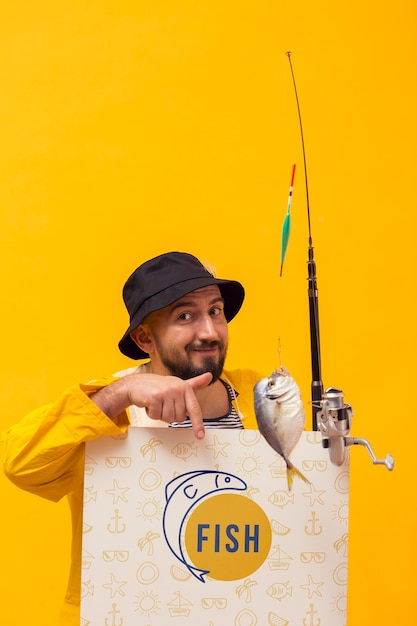 Pescador na capa de chuva, segurando a haste com peixe