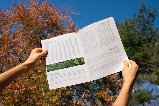 PSD pessoa segurando revista de papel ao ar livre na natureza