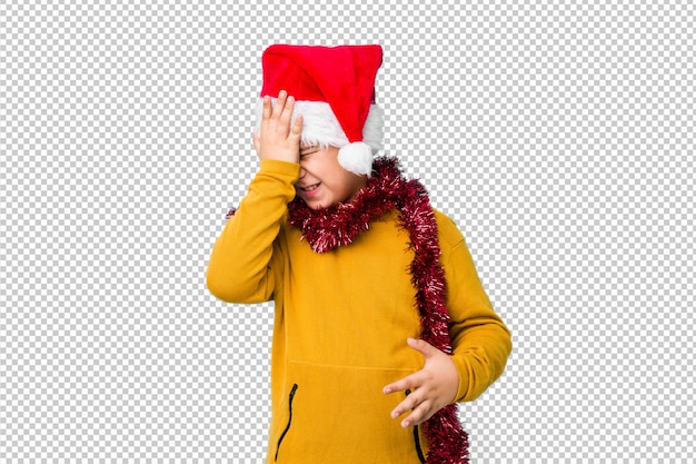 Petit garçon célébrant le jour de Noël portant un bonnet de Noel isolé oubliant quelque chose, giflant le front avec palme et fermant les yeux.