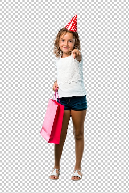 PSD petite fille à une fête d'anniversaire tenant un sac cadeau pointe le doigt vers vous