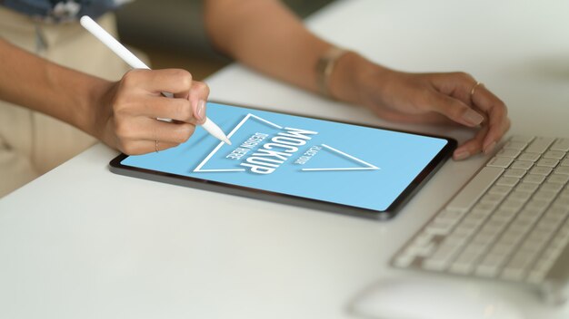 PSD photo recadrée de main féminine dessin sur maquette tablette avec stylet sur table d'ordinateur dans la salle de bureau