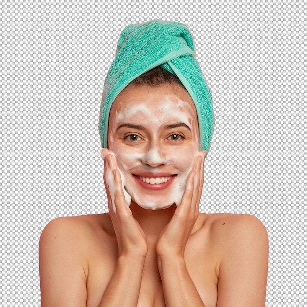 Positive young female has toothy smile has perfect teeth pats skin with liquid sanitary soap washes with foaming gel wakes up in morning for having beauty routine