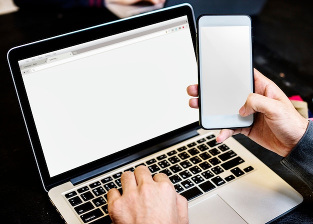 Primo piano delle mani che tengono telefono cellulare con il fondo del computer portatile del computer