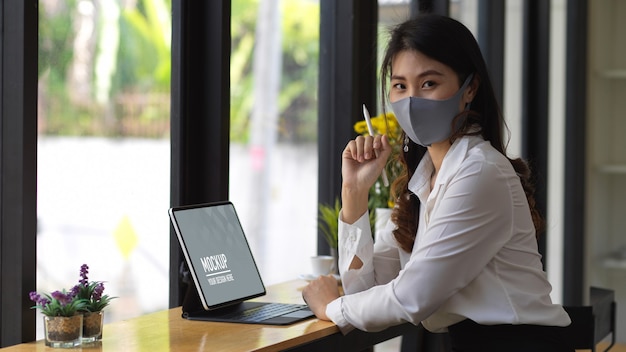 PSD retrato de mulher usando máscara enquanto trabalha com tablet digital em um café