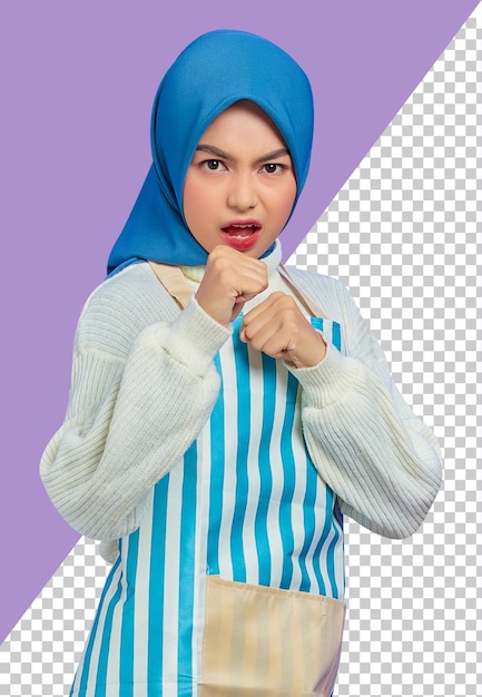 Retrato de uma jovem muçulmana asiática descontente em hijab e avental listrado em pé cerrando os punhos boxe e olhando câmera isolada no fundo roxo pessoas dona de casa conceito de estilo de vida muçulmano