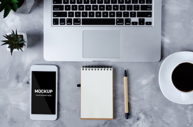 Smartphone branco com tela preta em branco na mesa de escritório com laptop e xícara de café