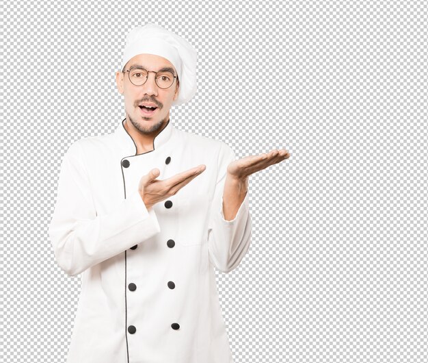 Sorprendido joven chef sosteniendo algo con su mano
