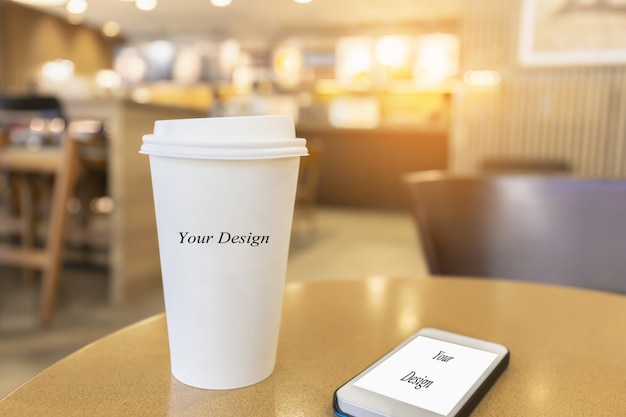 Taza de café caliente disponible con smartphone en una mesa de madera en el fondo de la cafetería