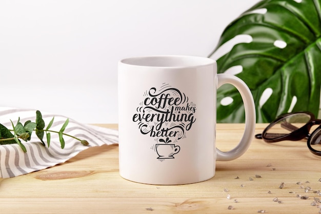 Taza de cerámica en escritorio de madera junto al mantel a rayas, cristales esparcidos y plantas verdes sobre fondo blanco.