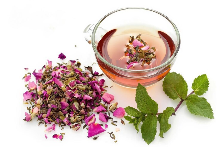 PSD una taza de té de hierbas con pétalos de rosa secos y hojas de menta frescas sobre un fondo blanco