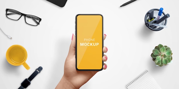 Téléphone intelligent dans la maquette de main de femme, au-dessus du bureau de travail. Vue de dessus, composition à plat