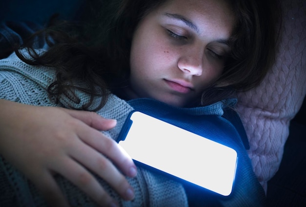 Uma rapariga a dormir com o telemóvel no peito.