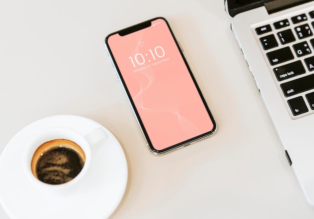 Un modello di telefono su un tavolo bianco con un portatile e una tazza di caffè