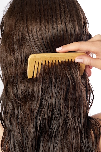 Una persona pettina delicatamente i capelli bagnati di colore marrone scuro usando un pettine di bambù a denti larghi