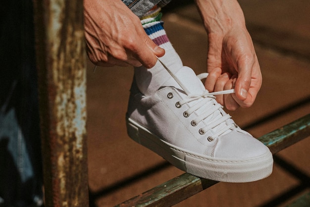 Uomo che aggiusta i lacci delle scarpe su un modello di scarpe da ginnastica bianche
