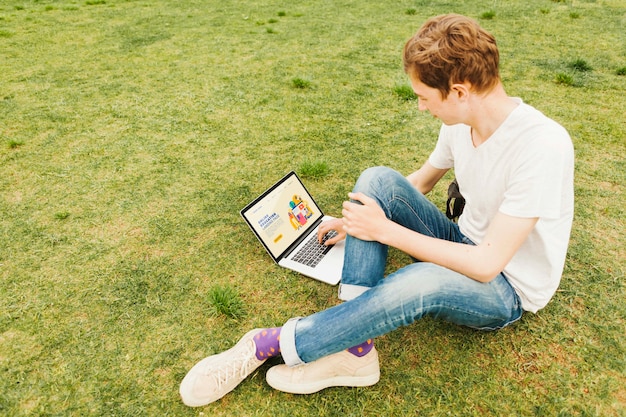 Varón joven que trabaja en la computadora portátil al aire libre