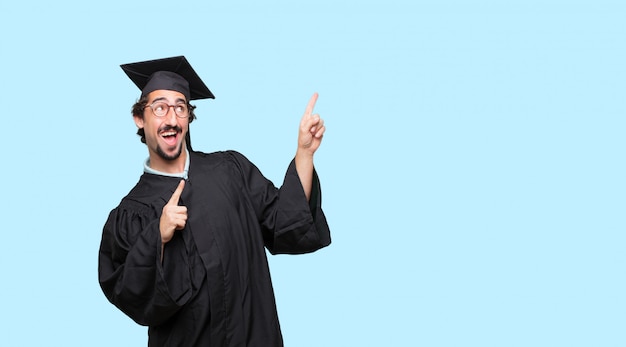 Victoria gesticular hombre joven graduado, con una mirada feliz, orgulloso y satisfecho en la cara