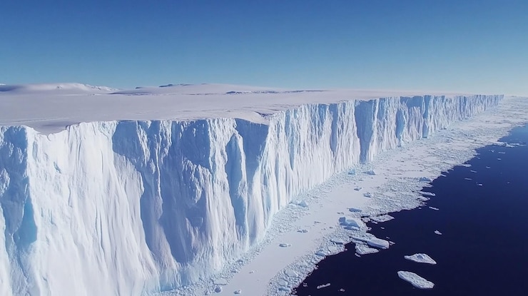 PSD vista aérea de un enorme acantilado de hielo antártico que se eleva sobre el oscuro agua del océano