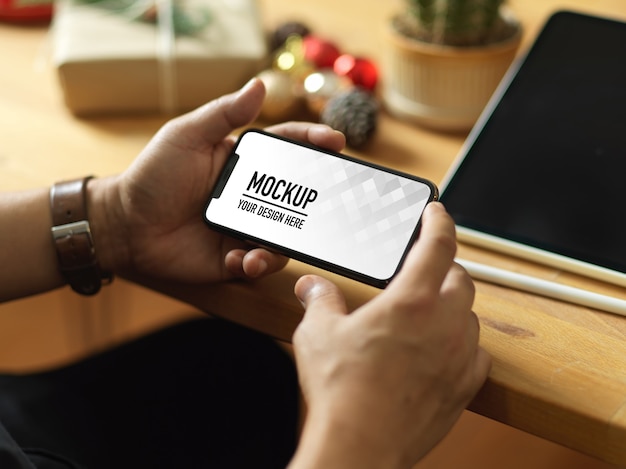 Vista dall'alto della mano che tiene il mockup dello smartphone e le decorazioni di Natale