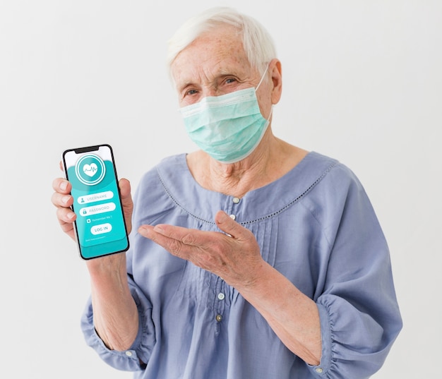 Vista frontal de una anciana con máscara médica con smartphone