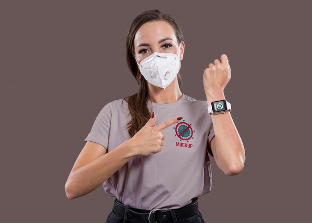 Vista frontal de mulher com máscara apontando para smartwatch