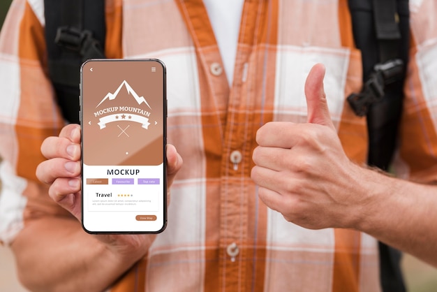 PSD vista frontal del hombre sonriente que sostiene el teléfono inteligente y que da los pulgares para arriba mientras acampa