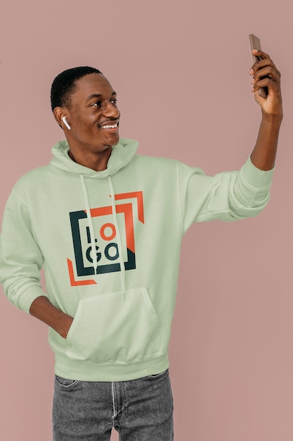 Vista frontale dell'uomo alla moda in felpa con cappuccio con auricolari prendendo selfie