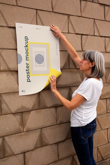 Vista de la persona pegando una maqueta de cartel exterior en la pared