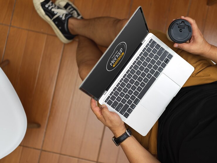 PSD vista superior de um homem relaxando em seu quarto enquanto segura a simulação de um laptop e uma xícara de café