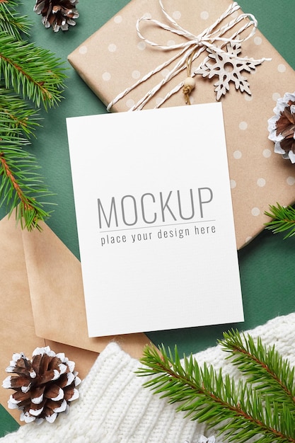 Weihnachtsgrußkartenmodell mit Geschenkbox, Kegeldekorationen und Tannenzweigen auf gestricktem Hintergrund