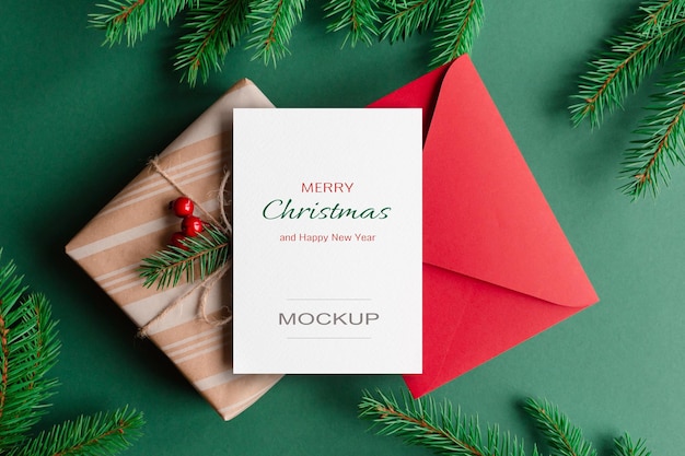 Weihnachtsgrußkartenmodell mit roter umschlaggeschenkbox und grünen tannenzweigen
