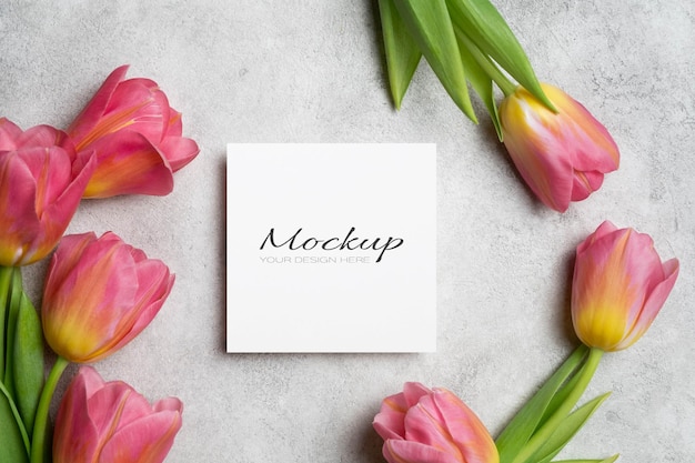 Weiße quadratische Einladung oder Grußkarte mit Tulpenblumen auf grauem Betongrund