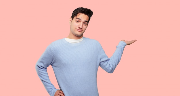 young handsome man smiling with a satisfied expression showing an object or concept