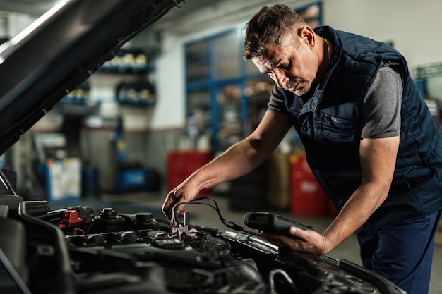 auto mechanic using diagnostic tool while checking car battery voltage in a workshop